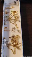 Photo showing the assorted gold-tone necklaces and various earrings in a box, some tangled, several single earrings and chains.