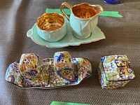 Photo showing entire set on table: leaf tray with sugar bowl and creamer; separate ornate salt and pepper shakers and tray in floral pattern.