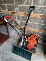 Electric snow shovel, plastic snow shovel, and extension cord together showing all included items for snow clearing.