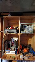 Wooden storage unit holding a variety of tools and accessories, showing multiple compartments with assorted items including a power tool and hand tools.