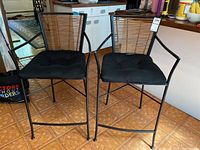 Pair of 2 metal frame bar stools with cane backs and black cushioned seats, shown together by kitchen counter.
