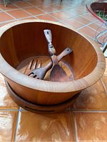 Wooden salad bowl containing two wooden tossers arranged crossed inside.