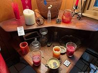 View of two wooden shelves holding various candles, candle holders, glass jars, a decorative container with lid, and a small ash tray.