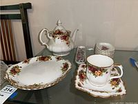 Full lot showing teapot, large platter, cup on saucer, and side dishes arranged on a glass table
