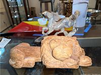 Front view showing both items, horse figurine behind lion head carving.