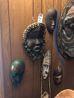 Photo showing six folk craft masks mounted on wall and one large woven circular bag or mat.