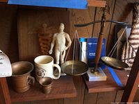 Photo showing medical anatomical model, ceramic mug, brass caduceus plaque, copper mugs, brass balance scale and medical books