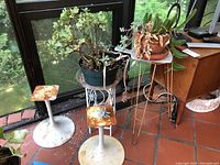 Photo showing two potted plants on separate rusted white-painted metal stands with natural light from window.