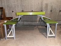 Full view of folding picnic table with two attached seats, showing folded metal frame and green plastic surfaces.