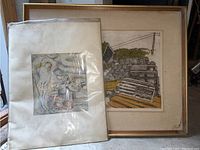 Two art pieces, one framed print and one matted print under plastic sleeve