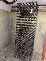 Full view of tall rectangular metal wine rack stored in a basement corner with concrete walls.