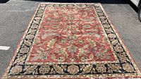 Full view of large rectangular wool area rug with floral and botanical patterns in red, black, green, and beige tones.
