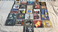 Collection of 25 CDs laid out in five rows visible in photo, showing various artists and bands with colorful album covers reflecting 80s and 90s music styles.