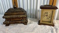Image showing both the carved wood trinket box and the Bulova clock placed side by side on a white fabric surface with vertical blinds background.