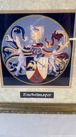 Colorful Enchelmayer coat of arms print in a gold-tone frame with black mat, featuring a lion, shield, and two animals supporting it.