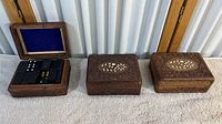 Three engraved wooden trinket boxes placed side by side on carpeted floor, one open showing blue felt lining and game pieces inside.