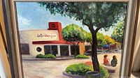 Frontal view of the framed painting depicting 'Le Boulanger' bakery with trees and people in front.