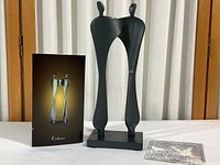 Full view of the black steel sculpture 'Partners' showing two stylized figures on a base, alongside brochure and Certificate of Authenticity on a white surface.