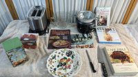 Full view of kitchen items including toaster, glass bowls, steamer pot, cookbooks, decorative plate, knife, and boxed citrus juicer