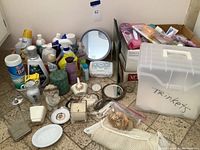 Photo showing assorted bathroom cleaning and personal care bottles, white plastic storage bin labeled "Trinkets", decorative candles, angel figurine, and two ornate hand mirrors.
