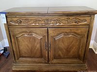 Frontal view of carved wooden sideboard with drawer and double doors, showing decorative floral carvings and paneled doors.
