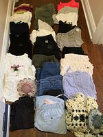 Photo showing assortment of women's clothing laid out, including jeans, pants, shirts, sweaters and scarves in various colors and fabrics.