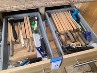 Kitchen drawers with wooden knife holders storing multiple knives and additional cooking tools and utensils.