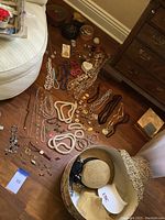 Full lot of costume jewelry including necklaces, bracelets, earrings spread on wooden floor with hats and hat box.