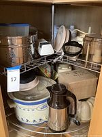 Kitchen appliances and bakeware items arranged in a kitchen cabinet shelf, showcasing crockpot, blender parts, baking dishes, and other utensils.