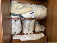 Photo of multiple folded blankets and sheets stored in a wooden cubby compartment showing various textures and neutral colors.