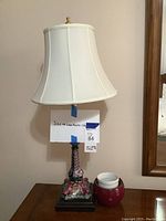 Full view of 32-inch tall decorative table lamp with cream shade and colorful hand-painted base on wooden platform.