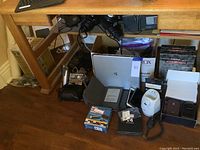 Multiple electronics and accessories on floor including Canon camera, Kindle, laptop, various phones, and other devices