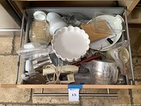 Top view of open drawer showing assortment of baking supplies including utensils, a glass pitcher, ceramic pie dish, and other kitchen items.