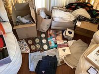 Wide view of the lot showing folded curtains, jeans, blankets, picture frames, fabric, and bags with items