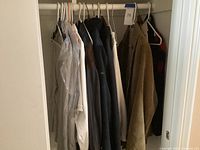 Image shows several men's jackets and coats hanging on hangers inside a closet rod; includes brown corduroy coat and dark jackets.