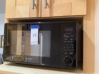 Front view of black Sharp Carousel microwave showing control panel and reflective door with logos.