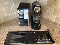 Nespresso coffee maker with manuals laid out next to the Coffee Stack pod holder on a tile kitchen counter.