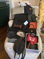 Photo showing assortment of handbags, purses, laptop bags, a large duffel bag and various smaller pouches and wallets on a chair.