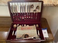 Photo showing full open wooden box containing Rogers silverplate utensil set, knives, forks, spoons in velvet-lined slots, plus additional serving utensils, guarantee paperwork included.