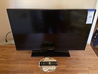 Front view of Samsung 32 inch television showing the screen and base stand with remote placed in front.