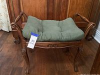 Front angled view of the wooden seating bench showing carved details and green cushion