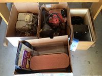 Photo of multiple cardboard boxes containing vintage hair dryer, sewing tool kit, books, speakers, plumbing parts, and other items.