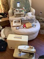 Singer sewing machine and hard carrying case in front of an ottoman with sewing kit boxes and supplies on top