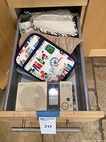 Open kitchen drawer containing Sony radio, colorful pot holder, multiple kitchen towels and cooking mitts in beige and cream tones.