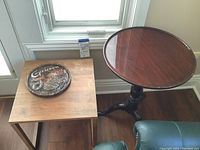 Two wood side tables placed on hardwood floor by window, with decorative Capricorn plate on smaller table