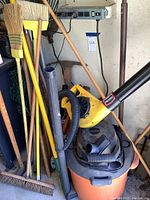 Photo shows Ridgid wet vac with orange and black body, Paramount yellow leaf blower with hose attachment, and various garden and cleaning tools surrounding them.