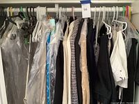 Wide view of assorted women's coats and jackets hanging on a closet rod with plastic protective covers on some items.