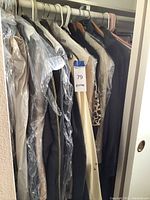 Closet view showing multiple coats and skirts on hangers, some in plastic garment bags, all in varying colors including black, beige, and cream.