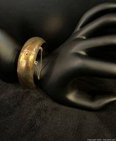 Side view of hinged 10 kt yellow gold bangle bracelet on black display hand, showing closure and safety chain.