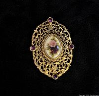 Front view showing oval filigree yellow gold brooch with four amethyst stones and central enamel rose accent inset